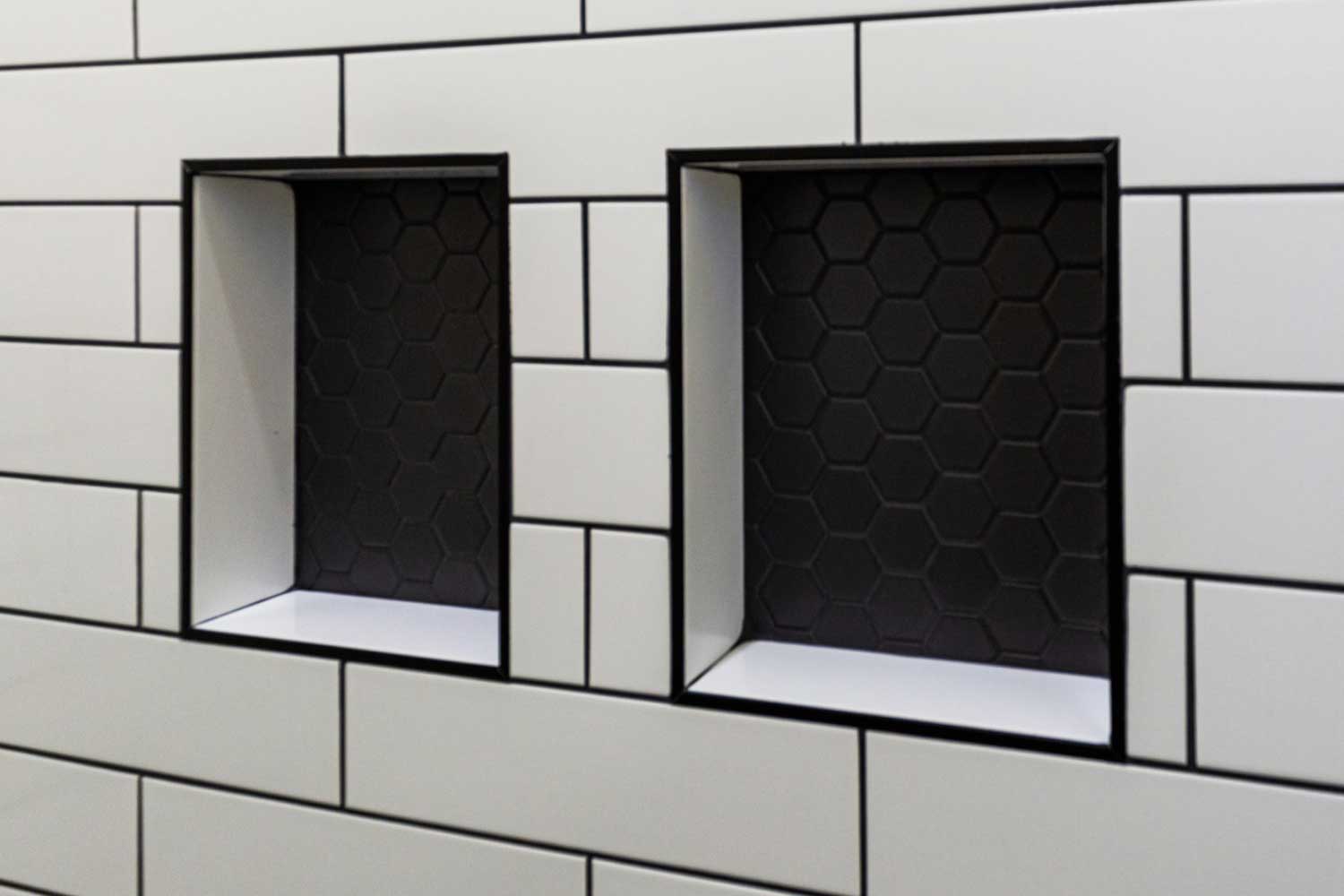 Close up of white tile shelves in the shower with black grout